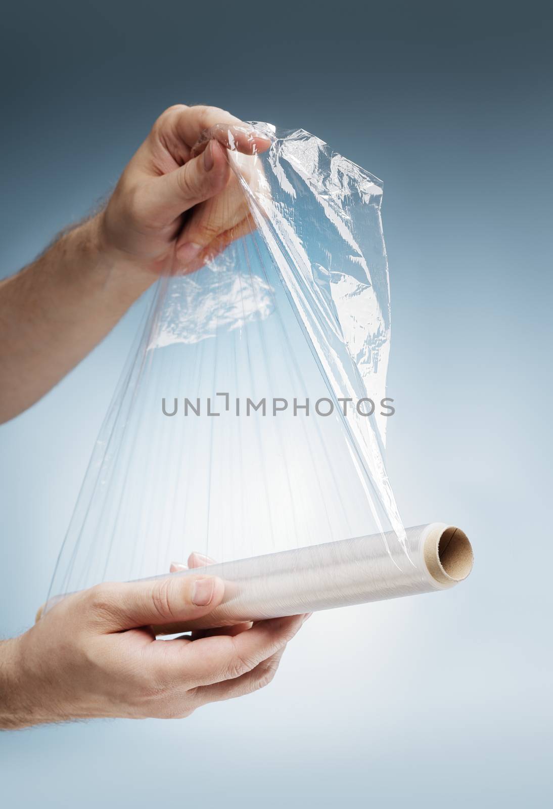 Man holding a roll of plastic film, typically used for sealing food items.