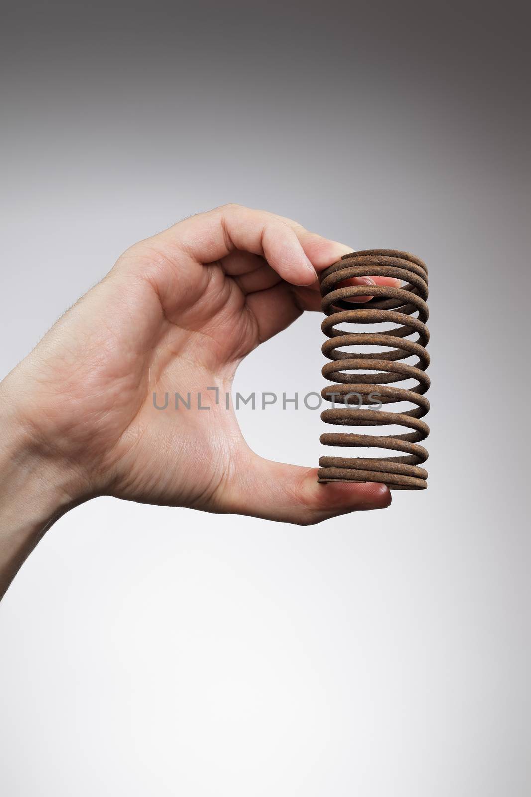 Man holding an old rusty spring is his hand.