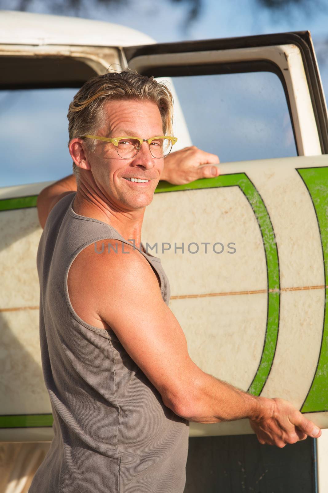 Single adult handsome man pulling surfboard out of his van