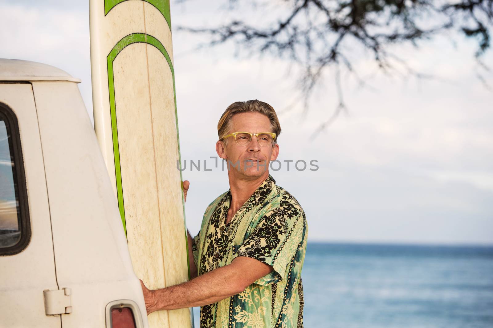 Optimistic man with eyeglasses holding a surfboard in Hawaii