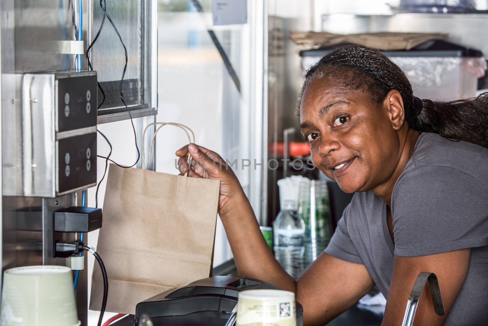 Smiling African-American worker hands order out window of modern food truck