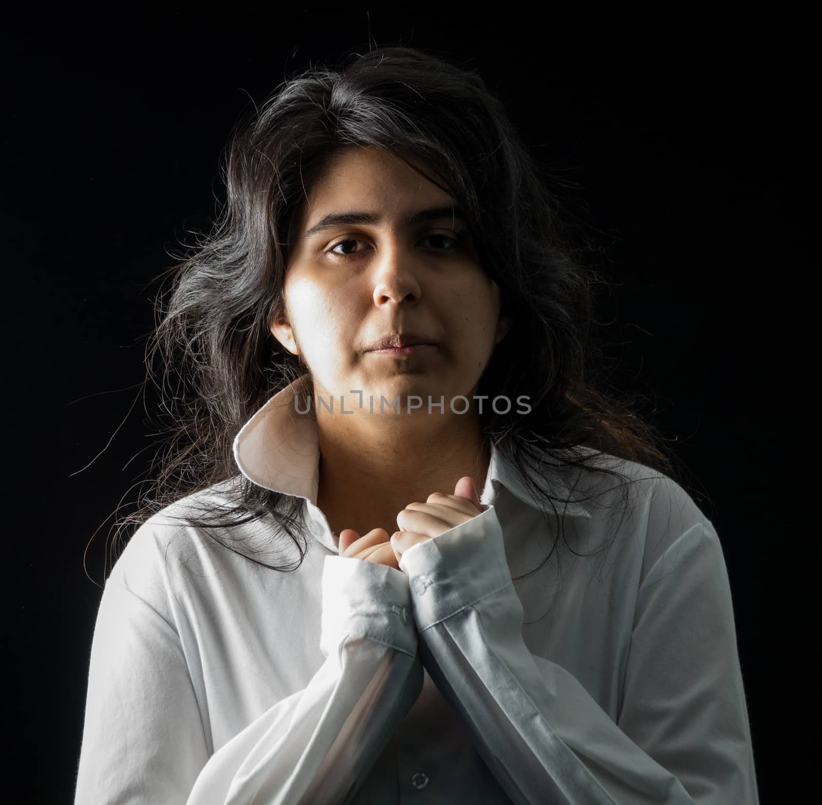 Latina teen in white long sleeved shirt standing in front of black backdrop
