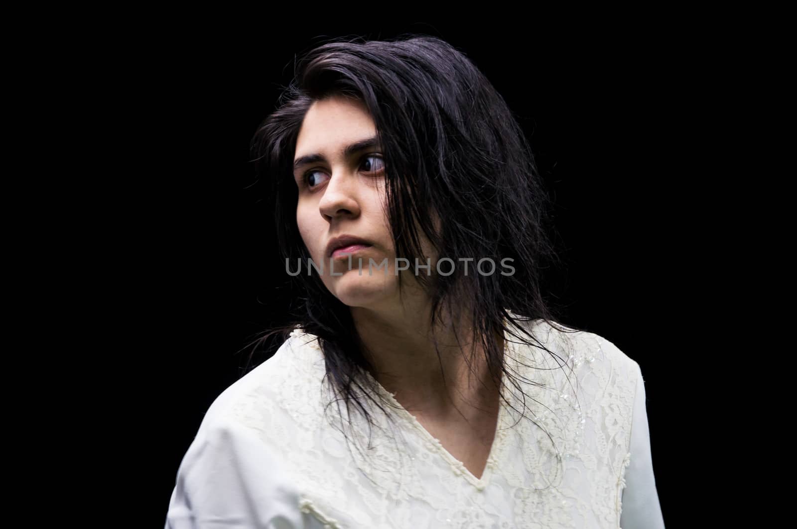 Latina teenager in white standing in front of a black background and looking over her shoulder with a serious expression on her face.