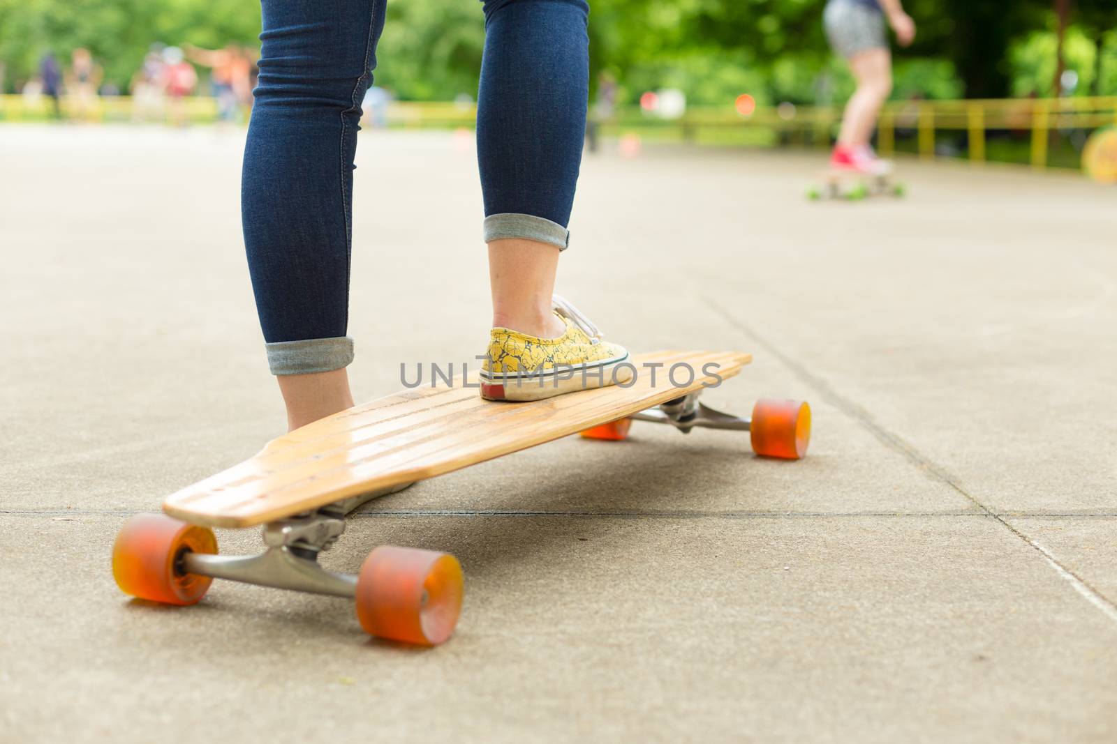 Teenage girl wearing blue jeans and sneakers practicing long board riding in skateboarding park. Active urban life. Urban subculture.