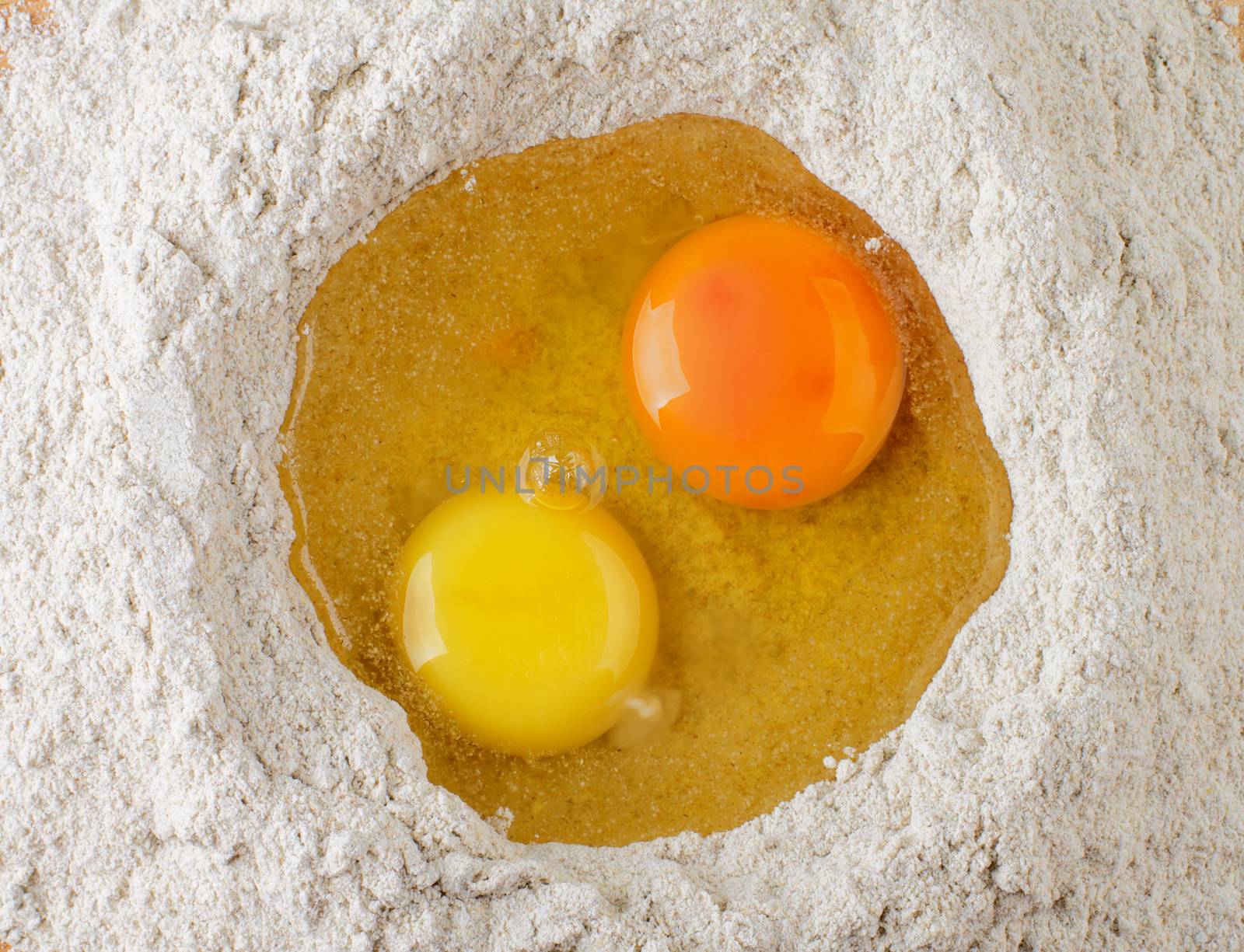 Two Light Yellow and Dark Yellow Egg Yolks into Heap of Whole Wheat Flour closeup. Top View