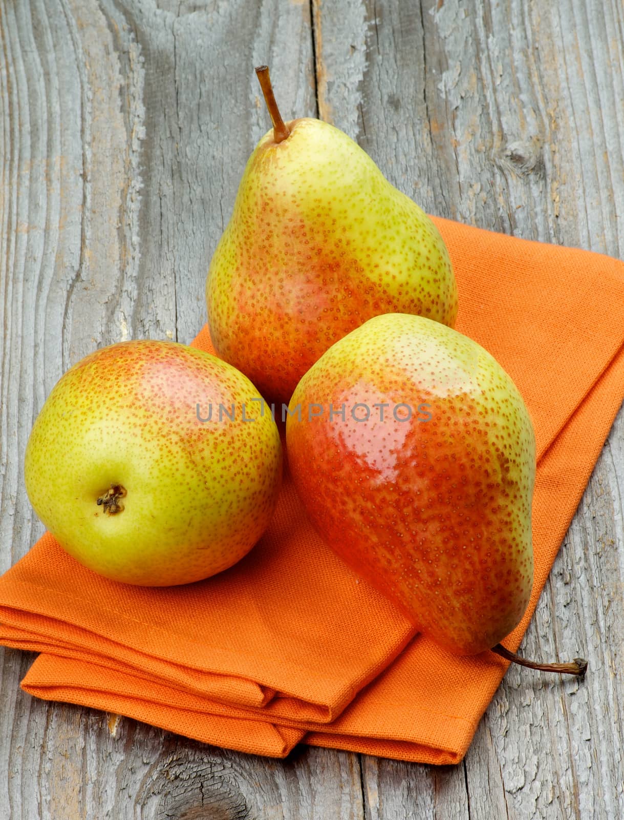 Three Ripe Yellow and Red Pears on Orange Napkin closeup on Rustic Wooden background