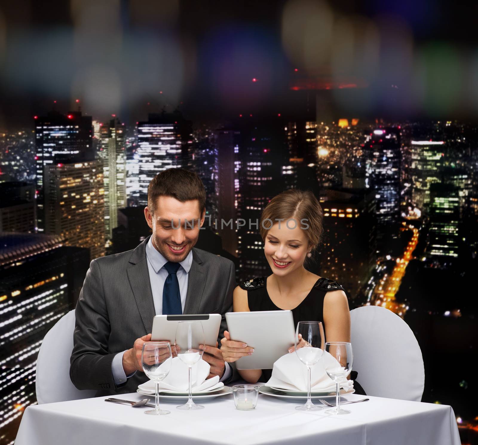 couple with menus on tablet pc at restaurant by dolgachov