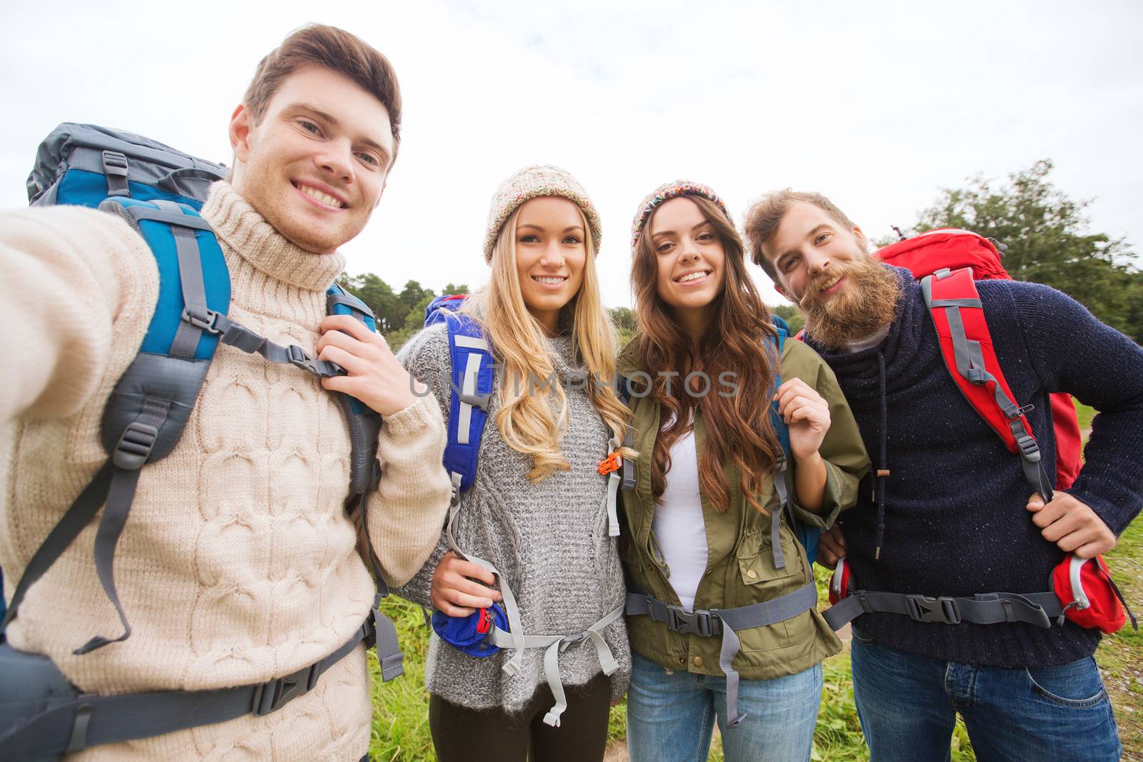 adventure, travel, tourism, hike and people concept - group of smiling friends with backpacks making selfie outdoors