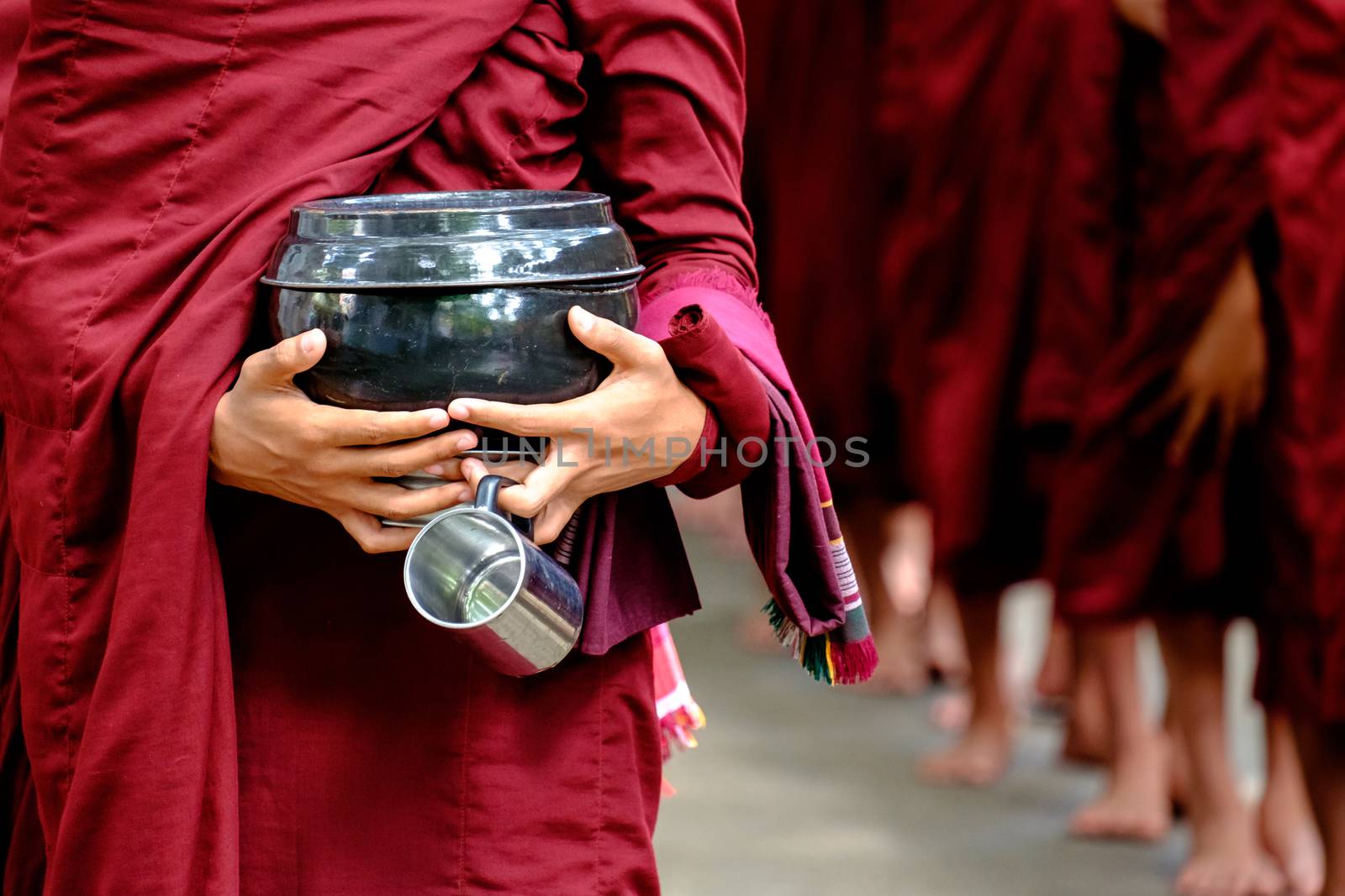 Detail of buddhist monks crowd in red robes and person holding a bowl and cup