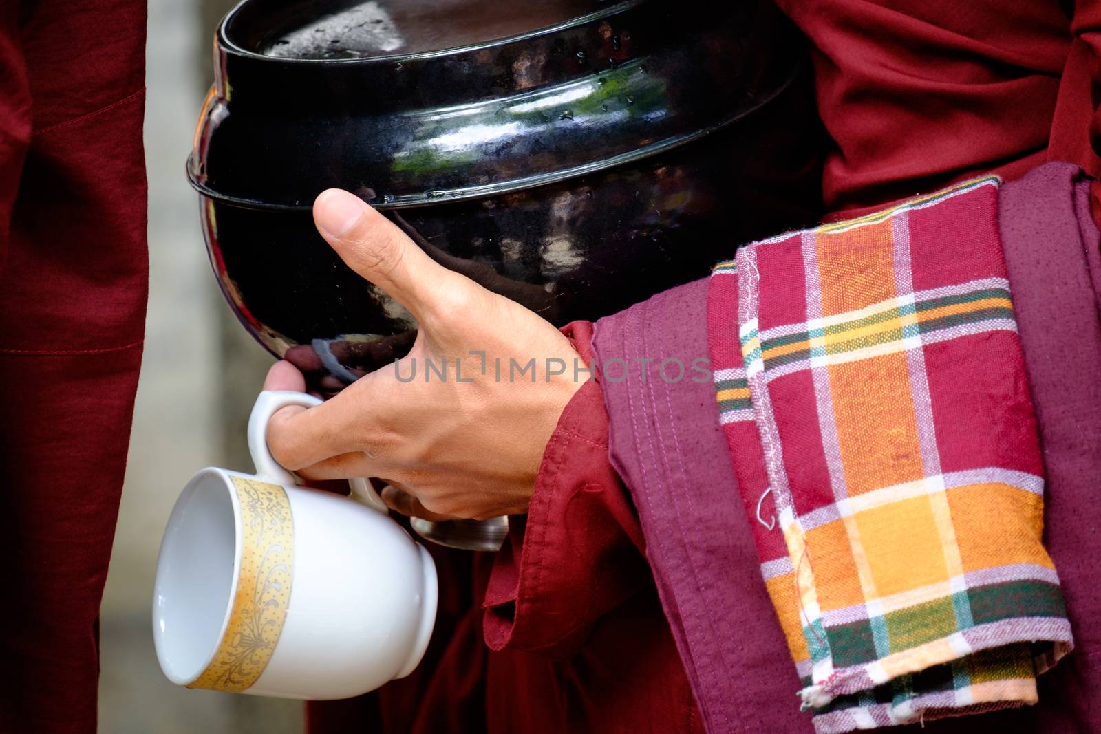 Detail of buddhist monk in red robe, his hands holding a bowl and cup