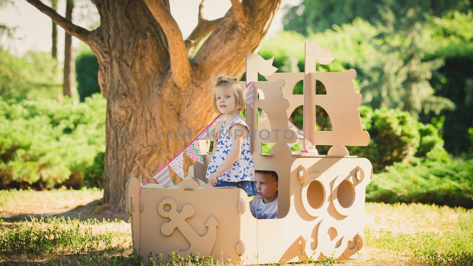 Boy and girl playing in a cardboard boat in the park. Eco concept