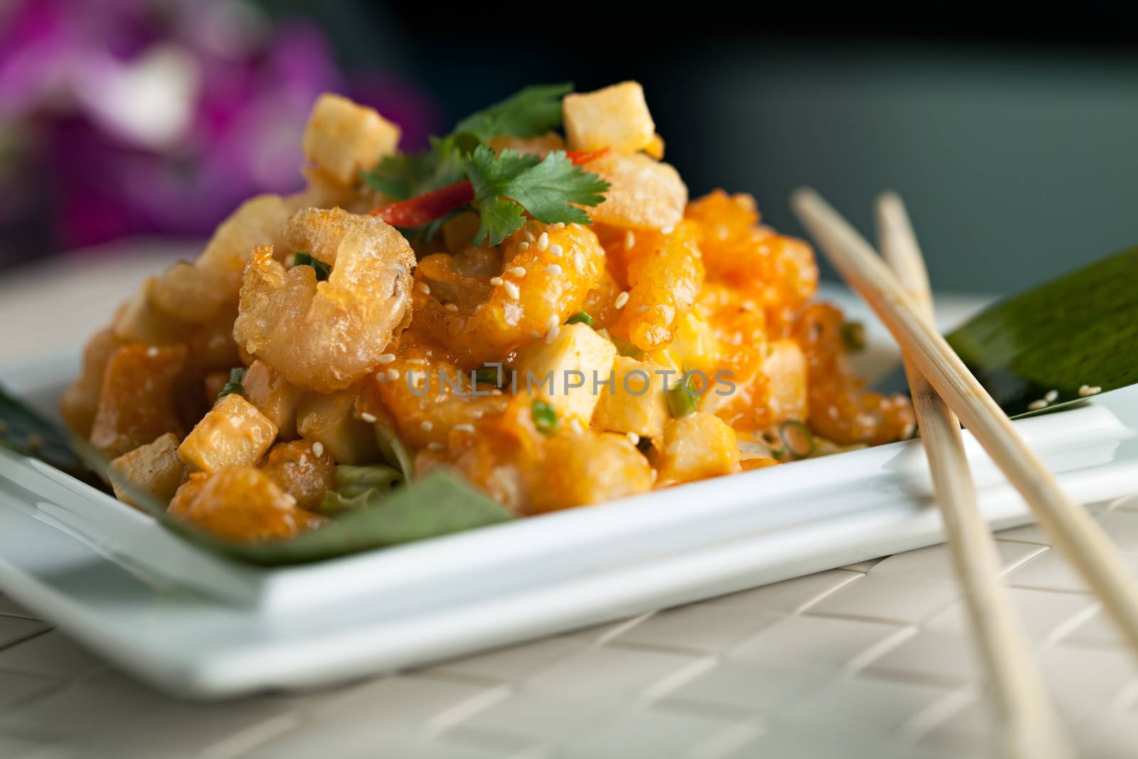 Thai crispy shrimp dish with apple and sesame seeds presented beautifully on a white square plate with chopsticks.  Shallow depth of field.