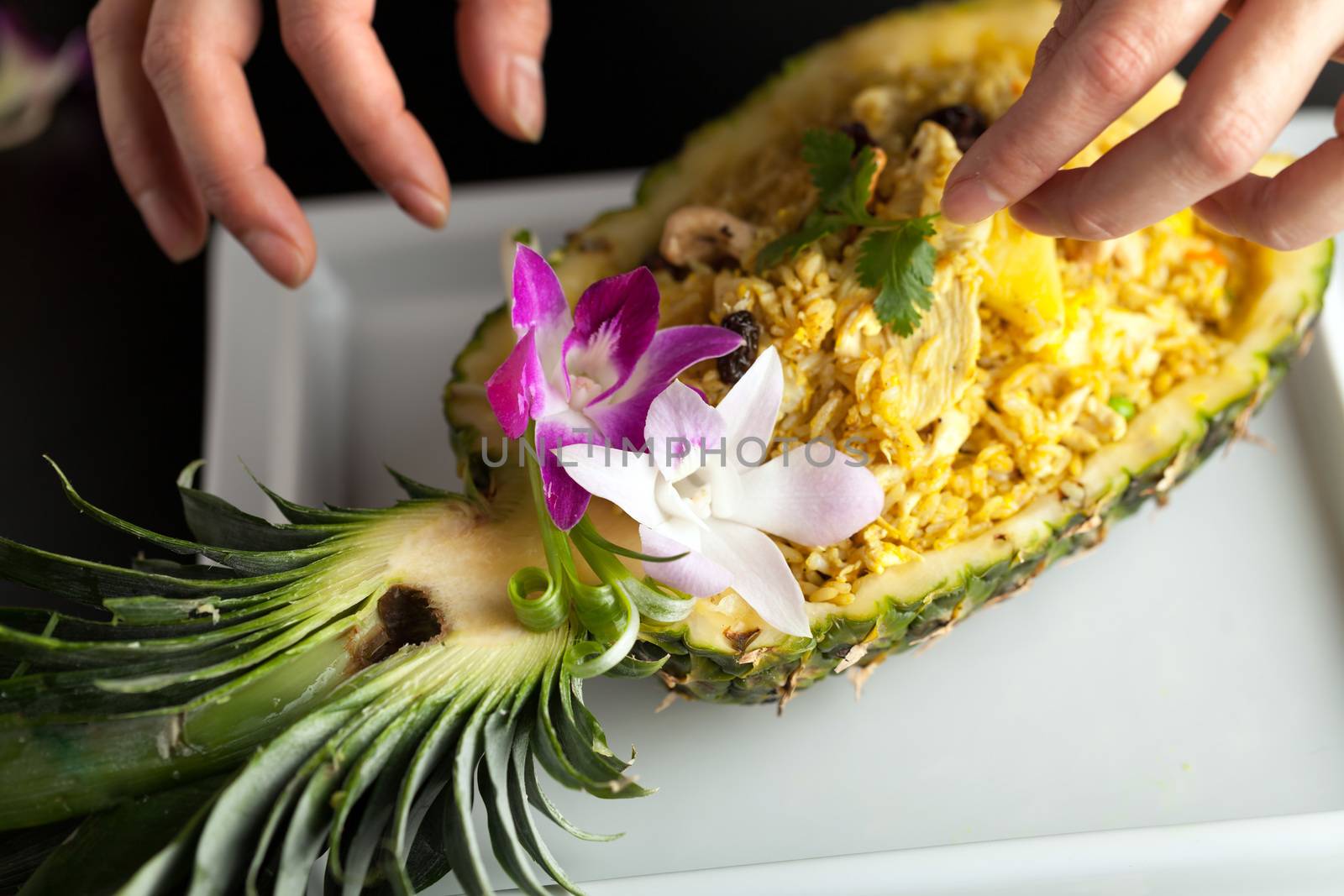 Freshly prepared pineapple fried rice served inside of a pineapple carved like a bowl. Food stylish is arranging garnish.