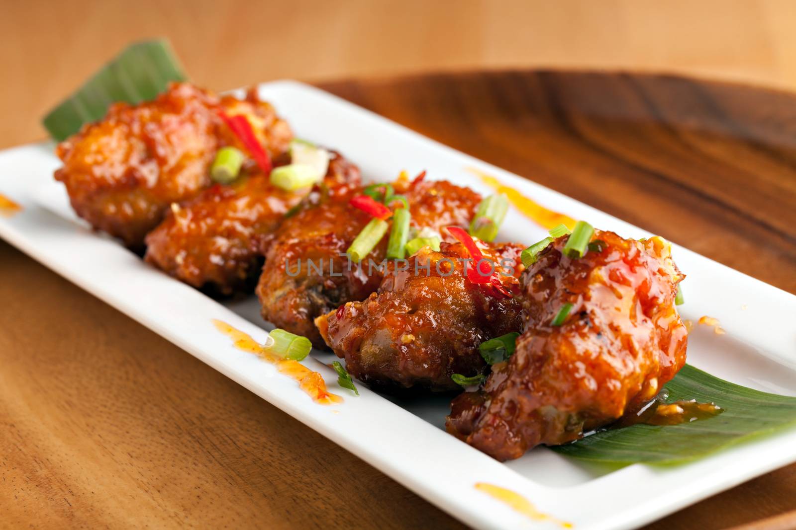 Thai style spicy chicken wings appetizer on a contemporary white plate.  Shallow depth of field.