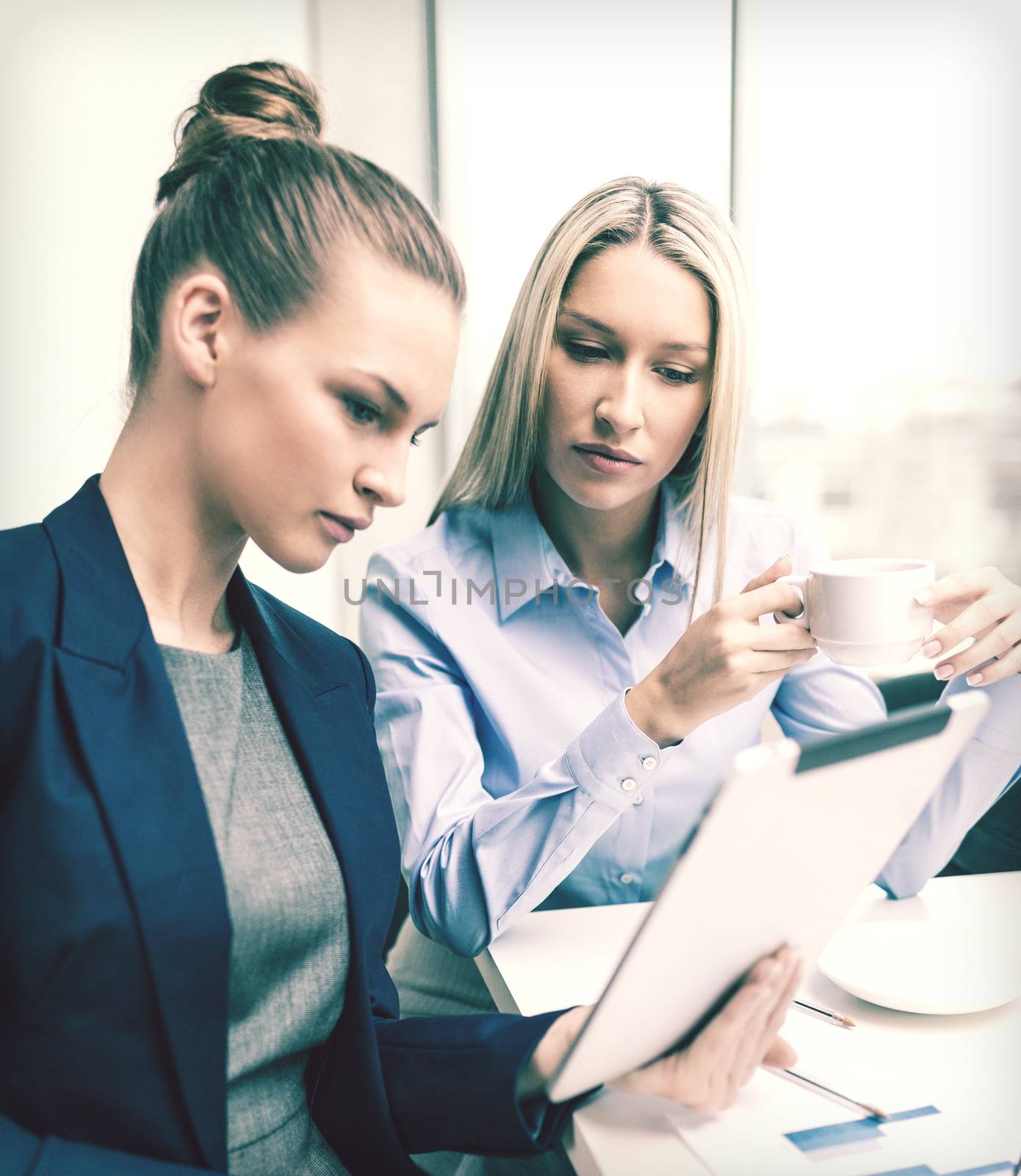 business, technology and office concept - serious businesswomen with tablet pc computers having discussion in office