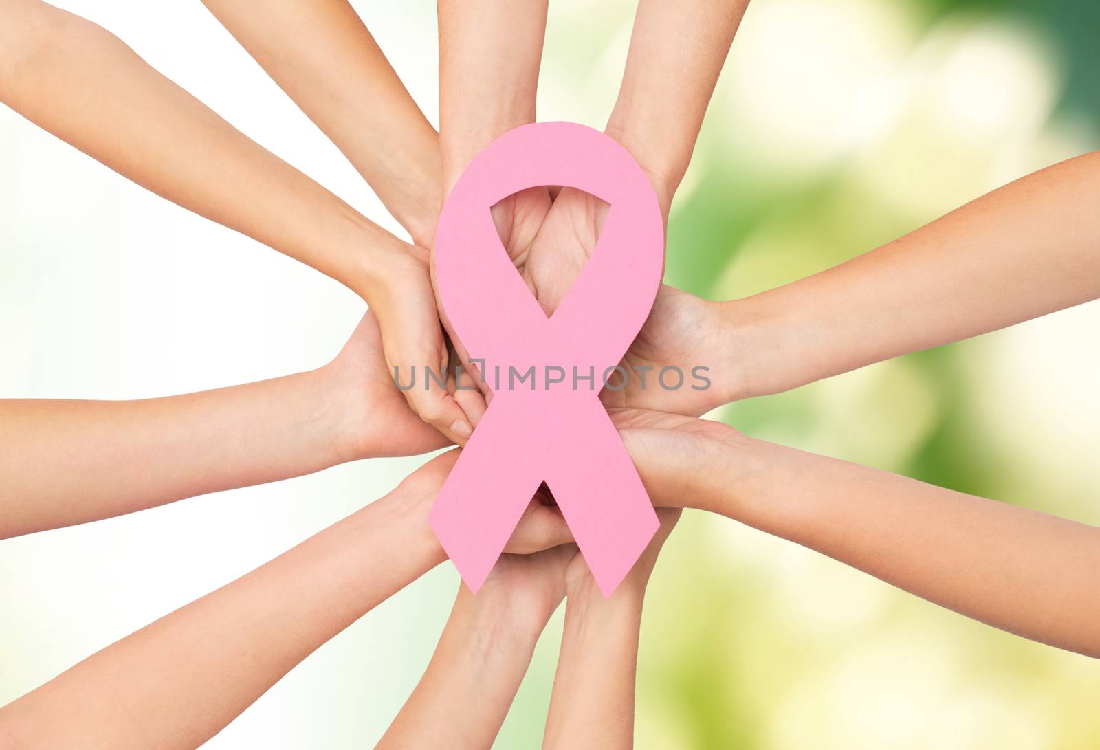 healthcare, people and medicine concept - close up of women hands with paper cancer awareness symbol over green background