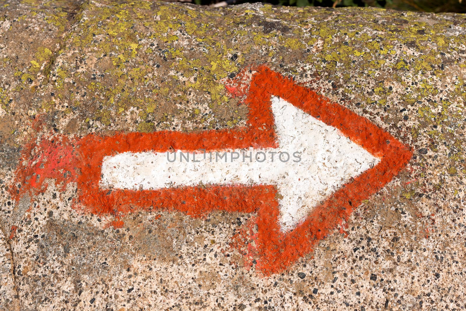 Red and white arrow painted on a rock of mountain. Hiking trail sign symbol in Italy alps