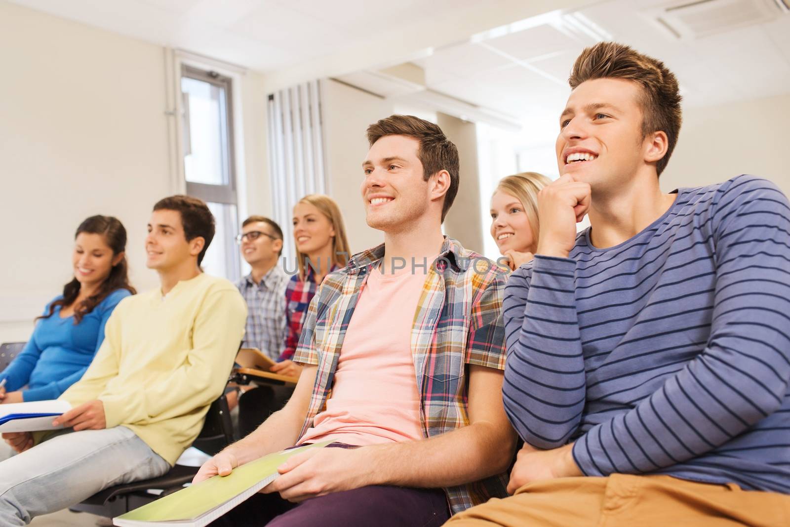 education, high school, teamwork and people concept - group of smiling students with notepads sitting in lecture hall