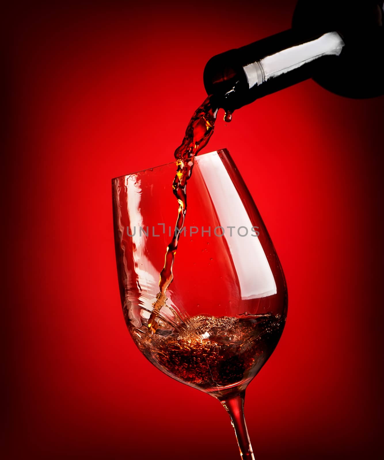 Red wine pouring in a wineglass on a red background