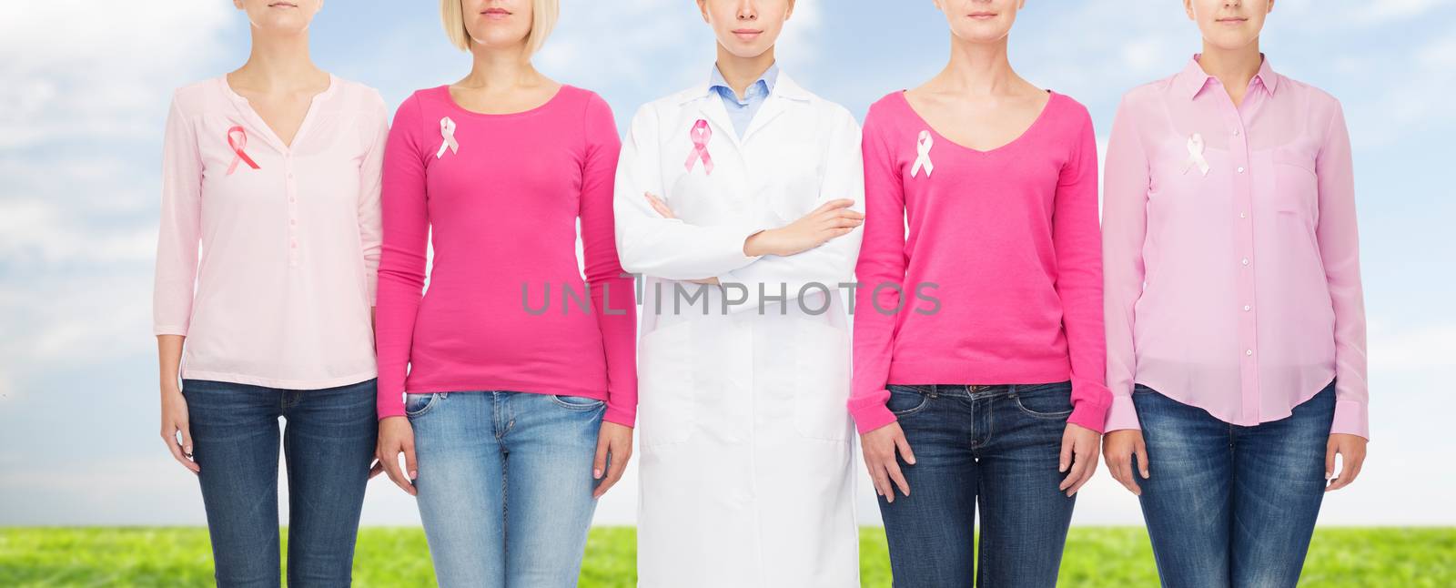 healthcare, people and medicine concept - close up of women in blank shirts with pink breast cancer awareness ribbons over blue sky and grass background