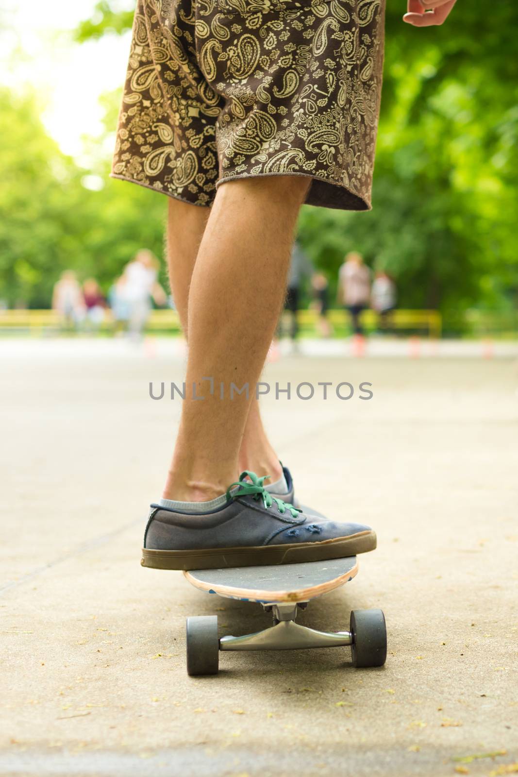 Guy wearing shorts and sneakers practicing long board riding in skateboarding park. Active urban life. Urban subculture.
