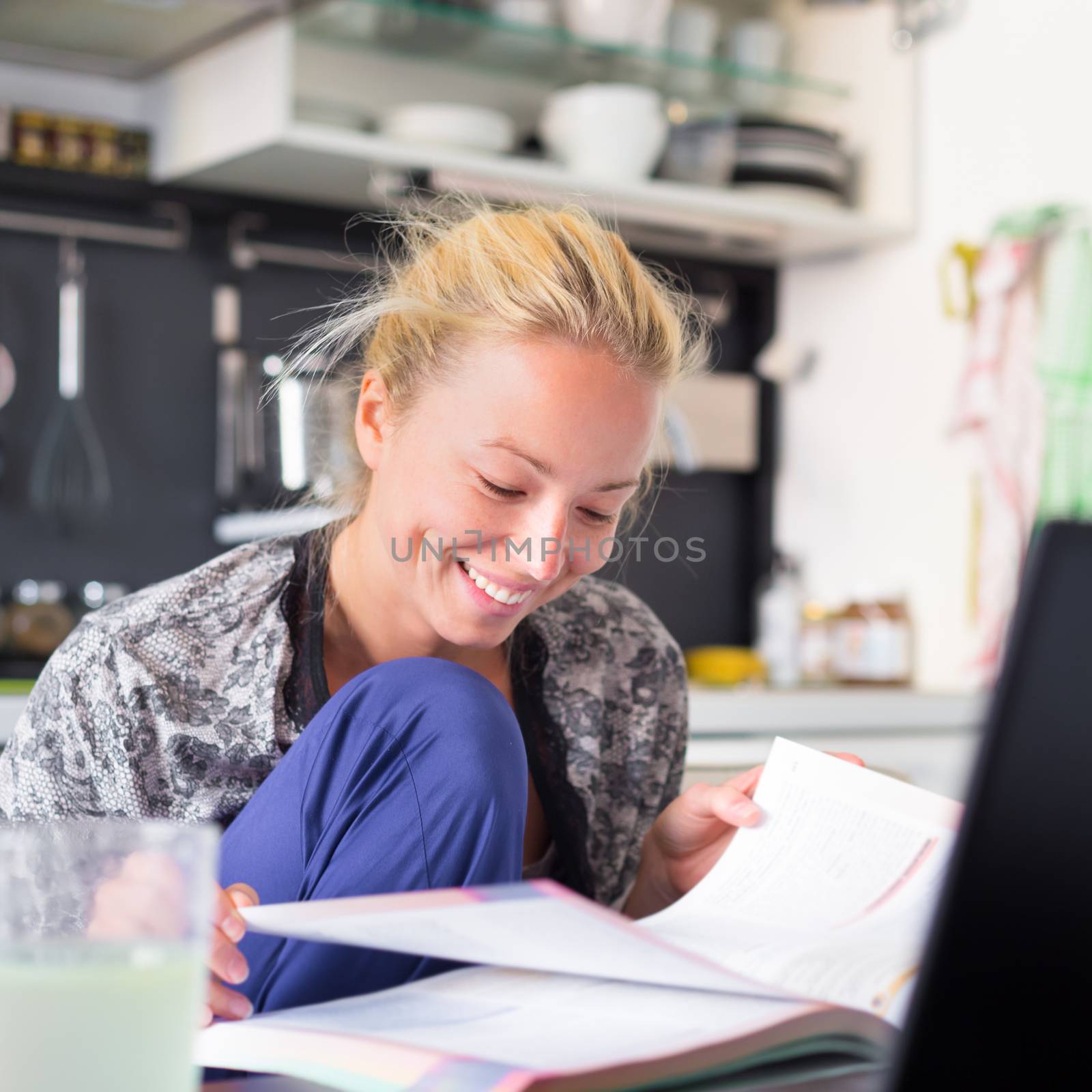 Female student in her casual home clothing working and studying remotly from her small flat in the morning. Home kitchen in the background. Great flexibility of web-based courses and study programmes.