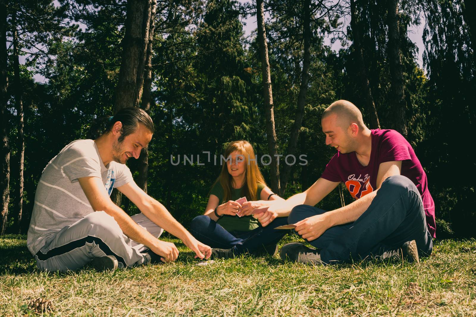 Three friend having fun by playing cards in the forest