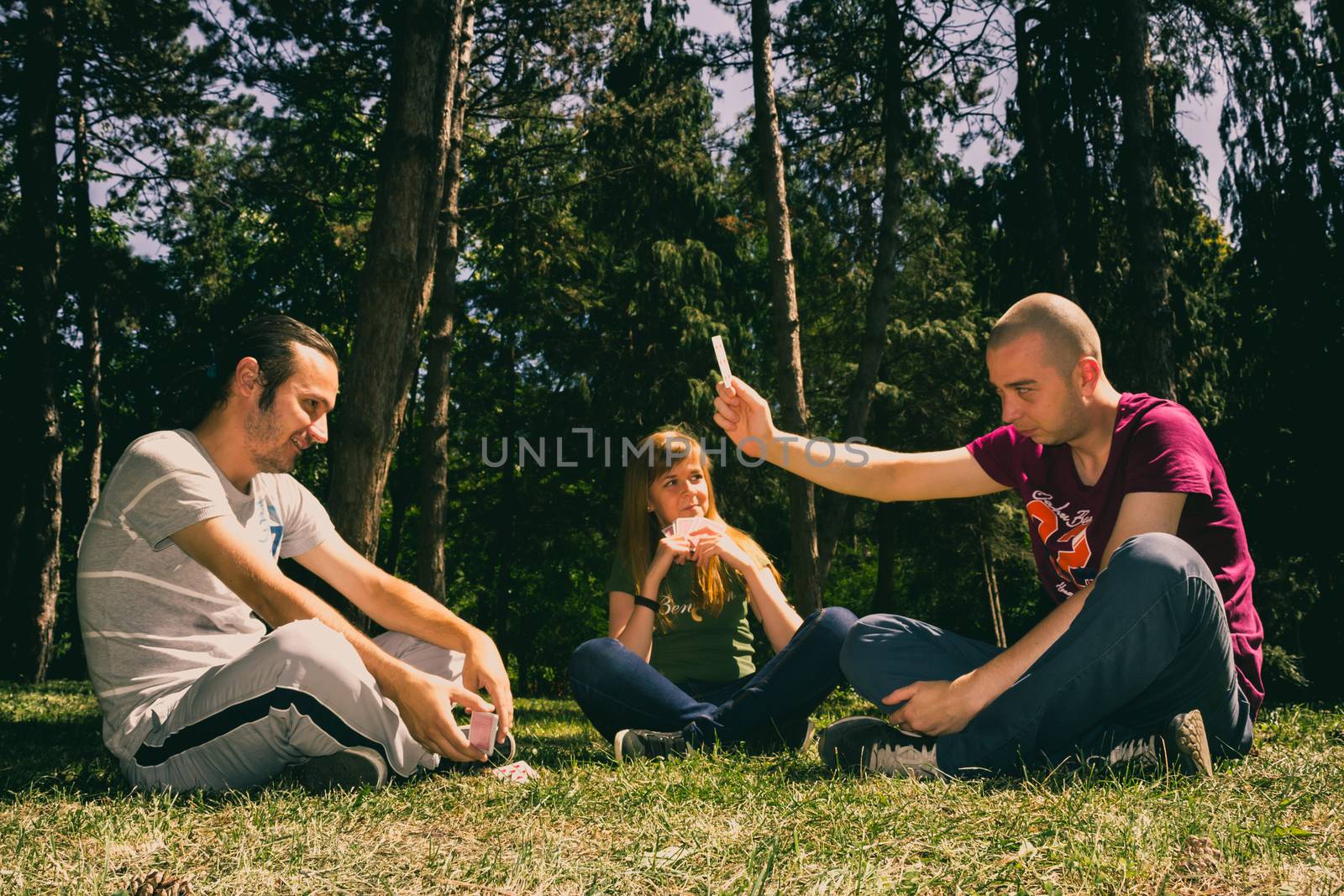 Three friend having fun by playing cards in the forest