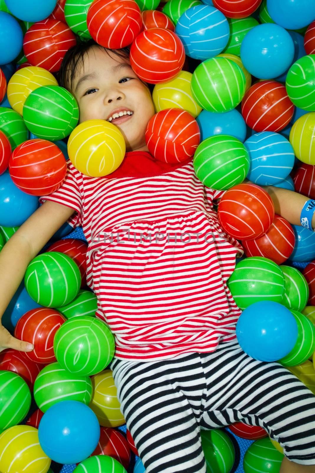 Asian Chinese girl hide in colorful ball pool at indoor playground.