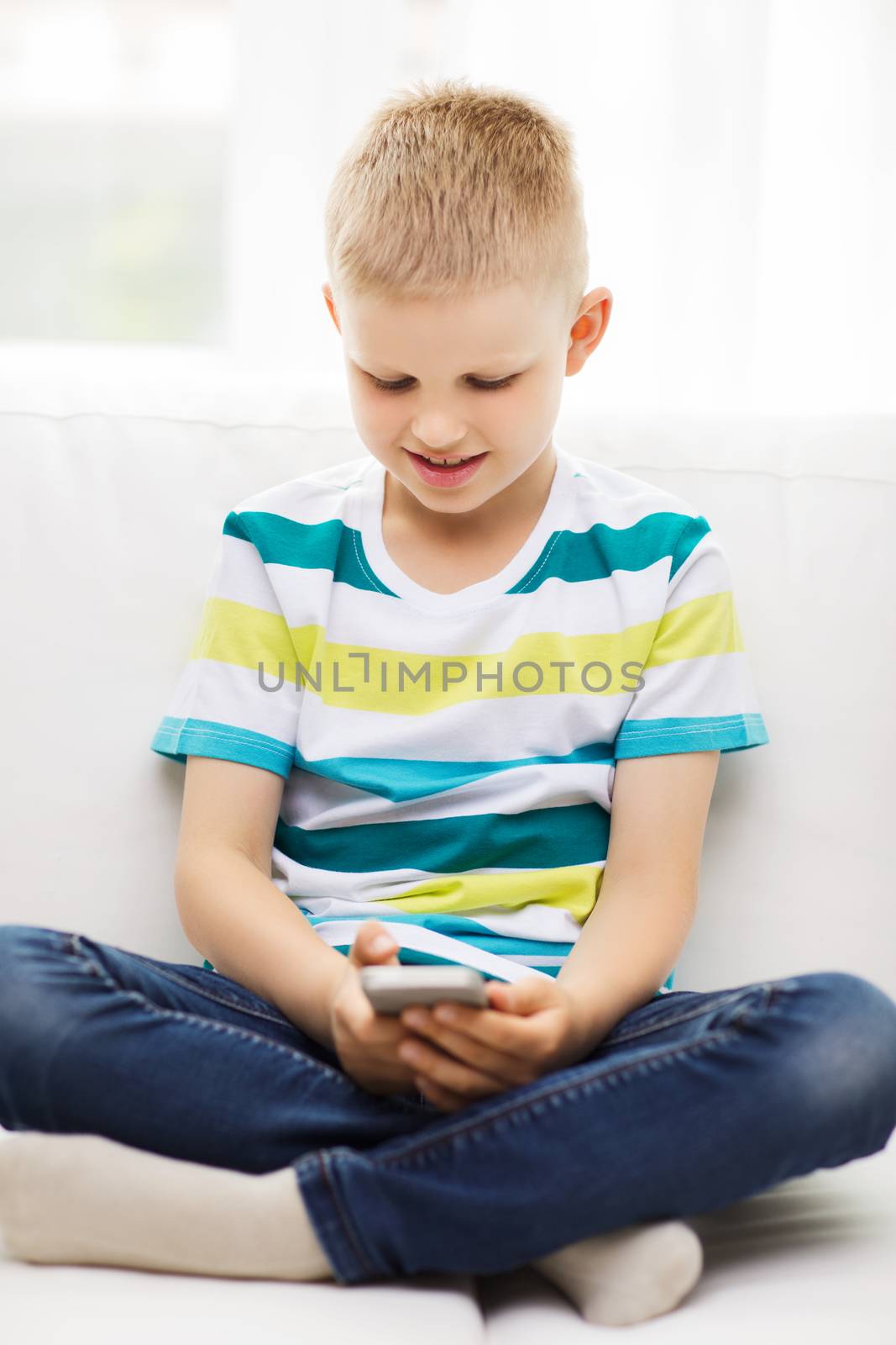 home, leisure, technology and internet concept - smiling little boy with smartphone at home