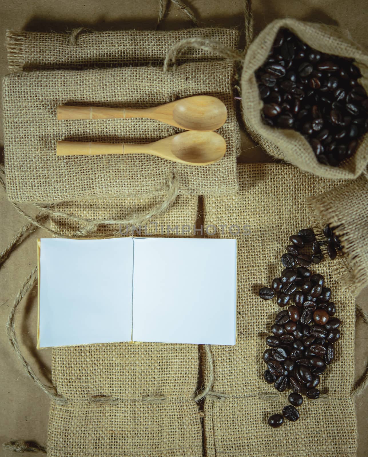 Notepad, wooden spoon and coffee beans on sack surface background.