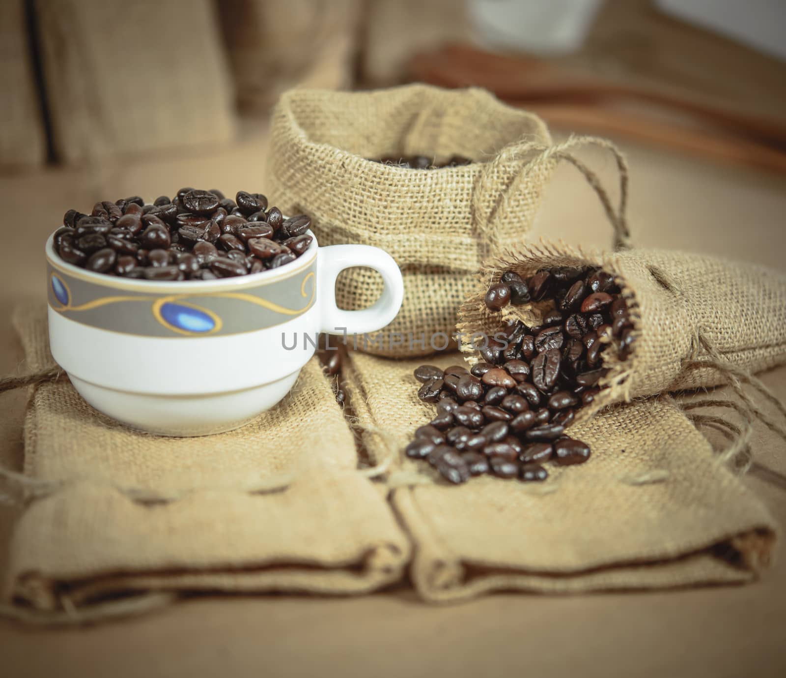 Vintage cup of roasted coffee beans on sack surface, Soft focus.