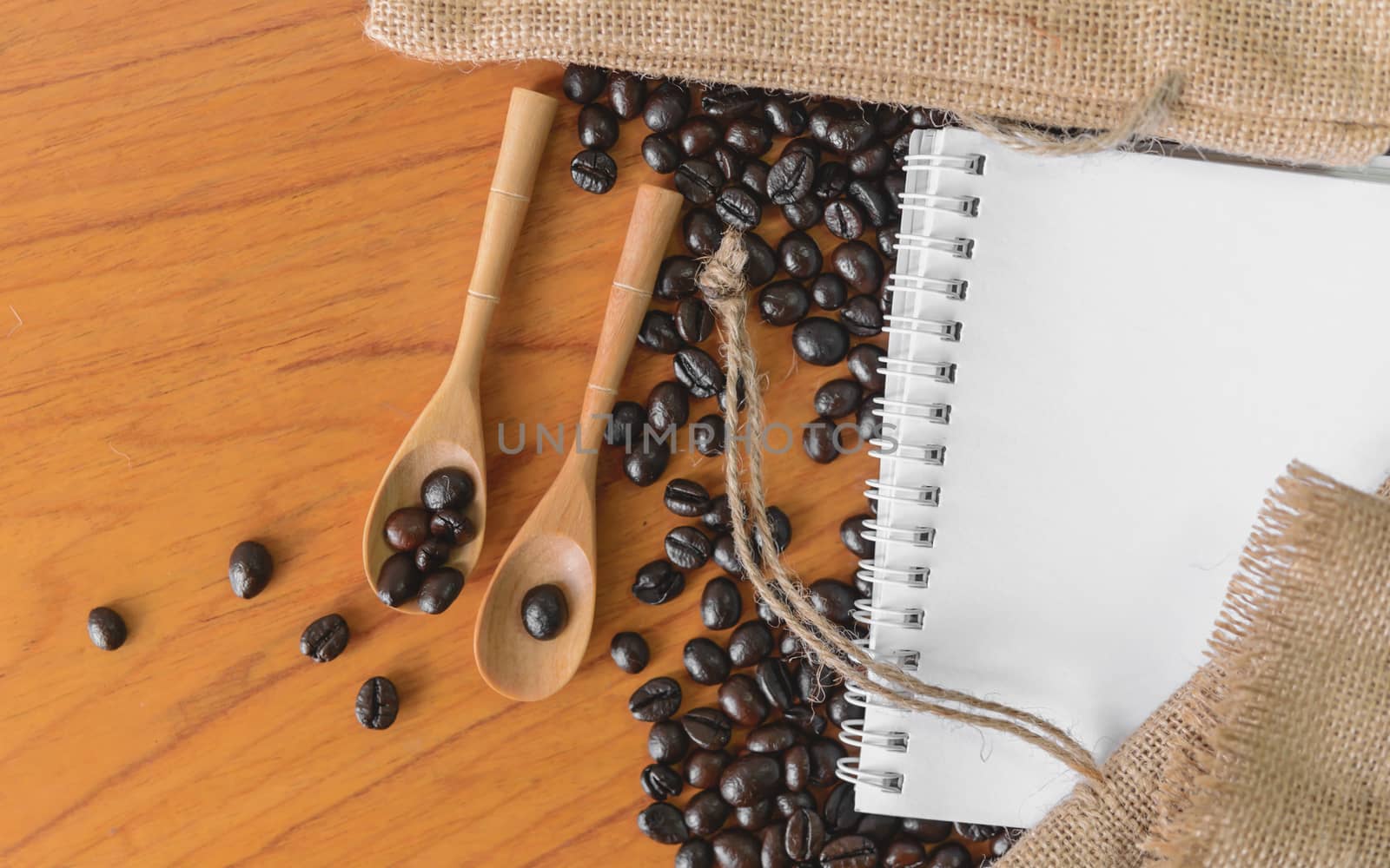 White notebook for your text with sackcloth and coffee beans on wooden spoon.