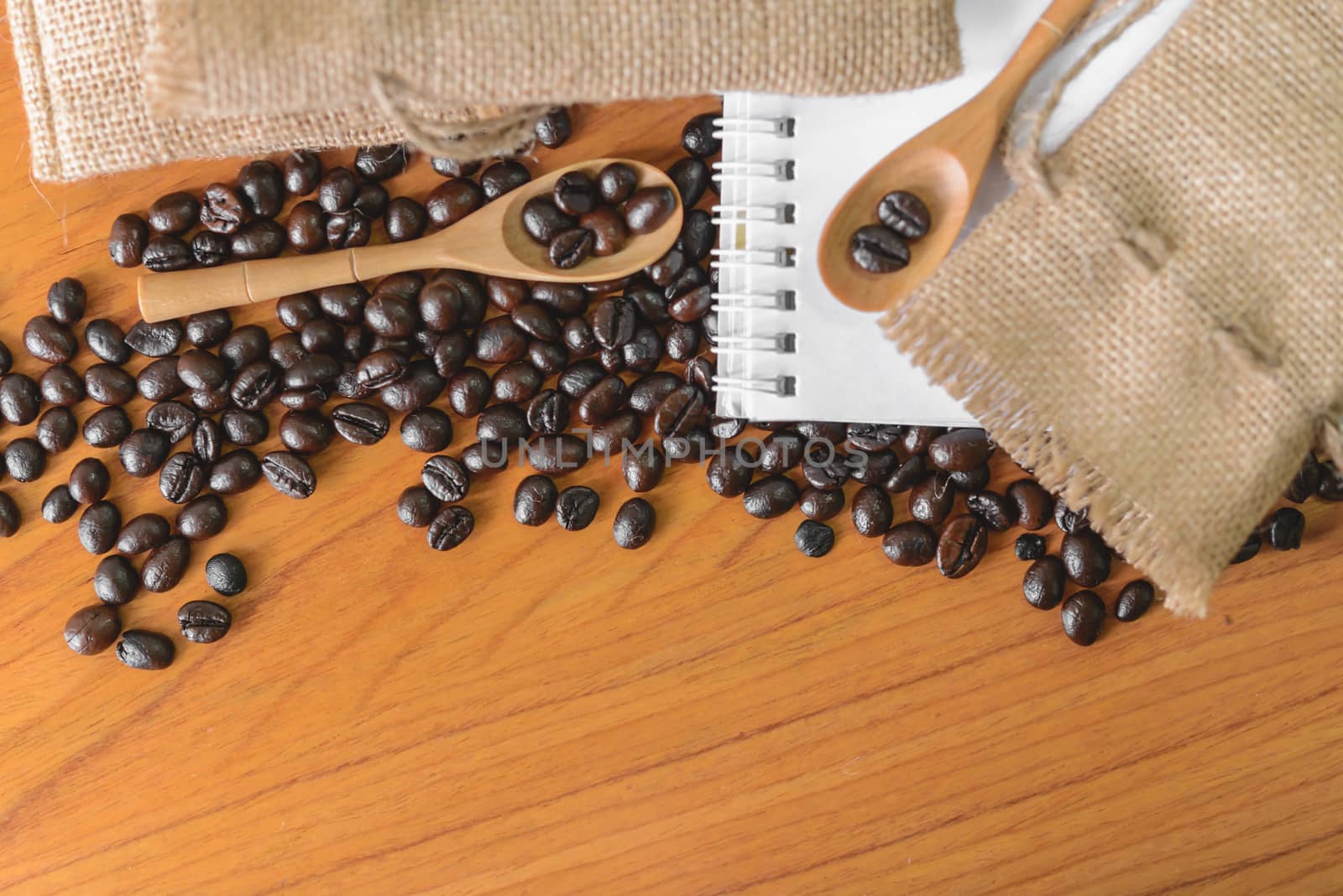 White notebook for your text with sackcloth and coffee beans on wooden spoon.