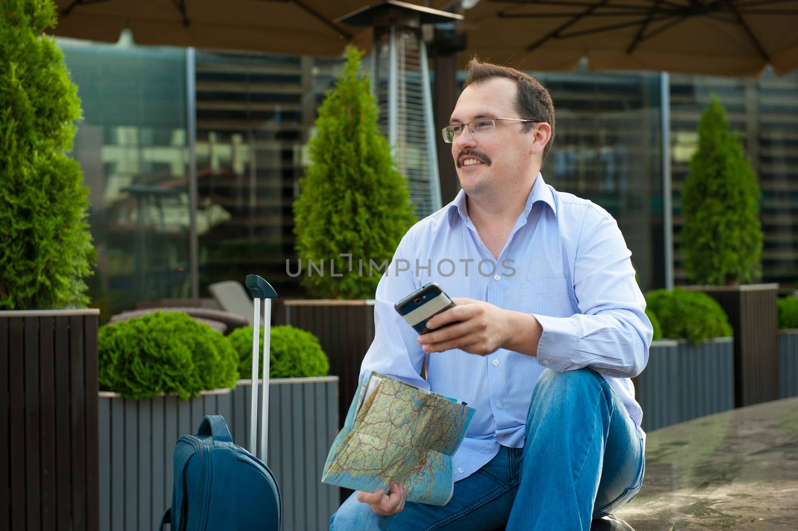 Traveler with mobile phone and city plan sitting outdoors.