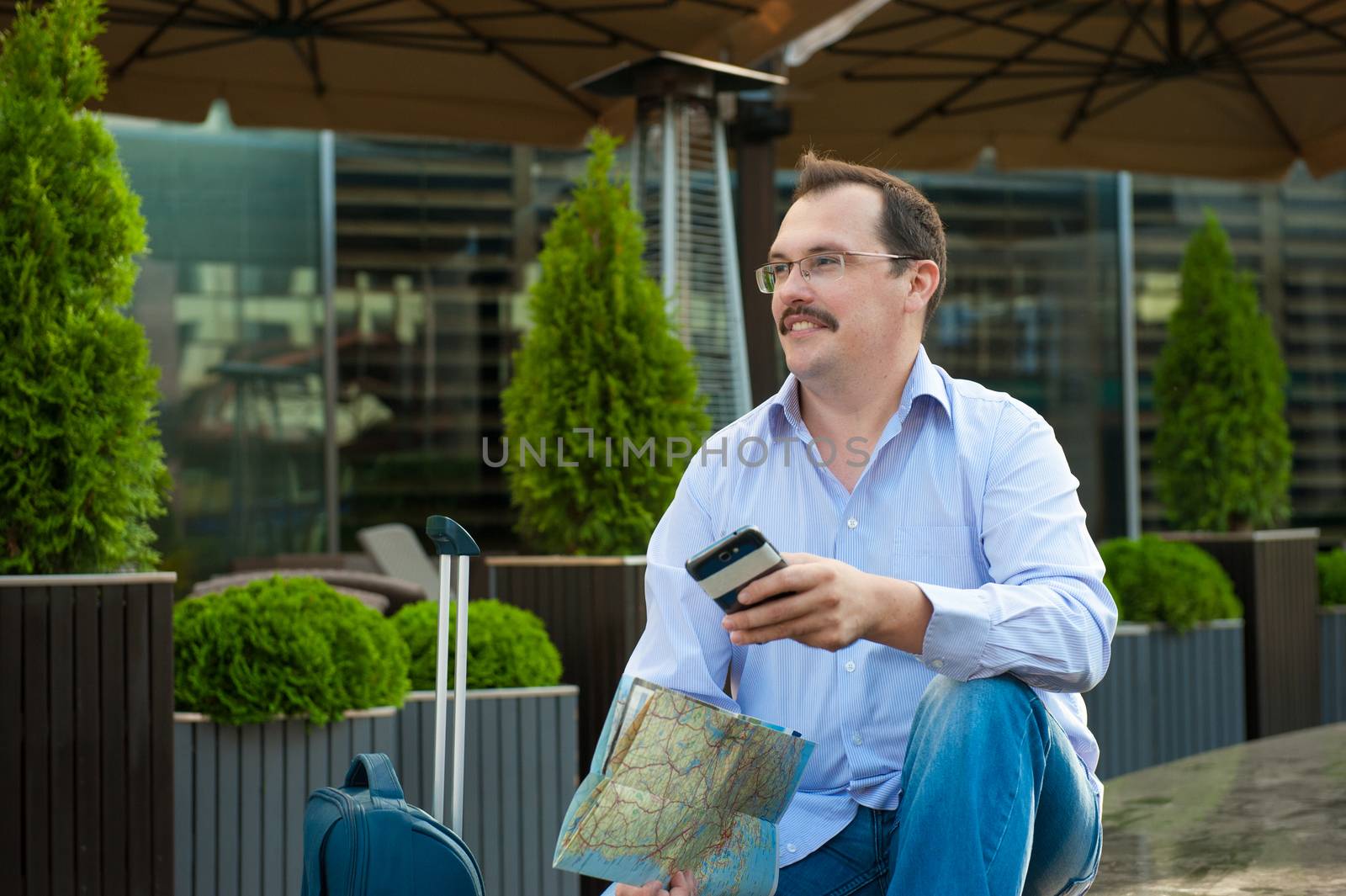 Traveler with mobile phone and city plan sitting outdoors.