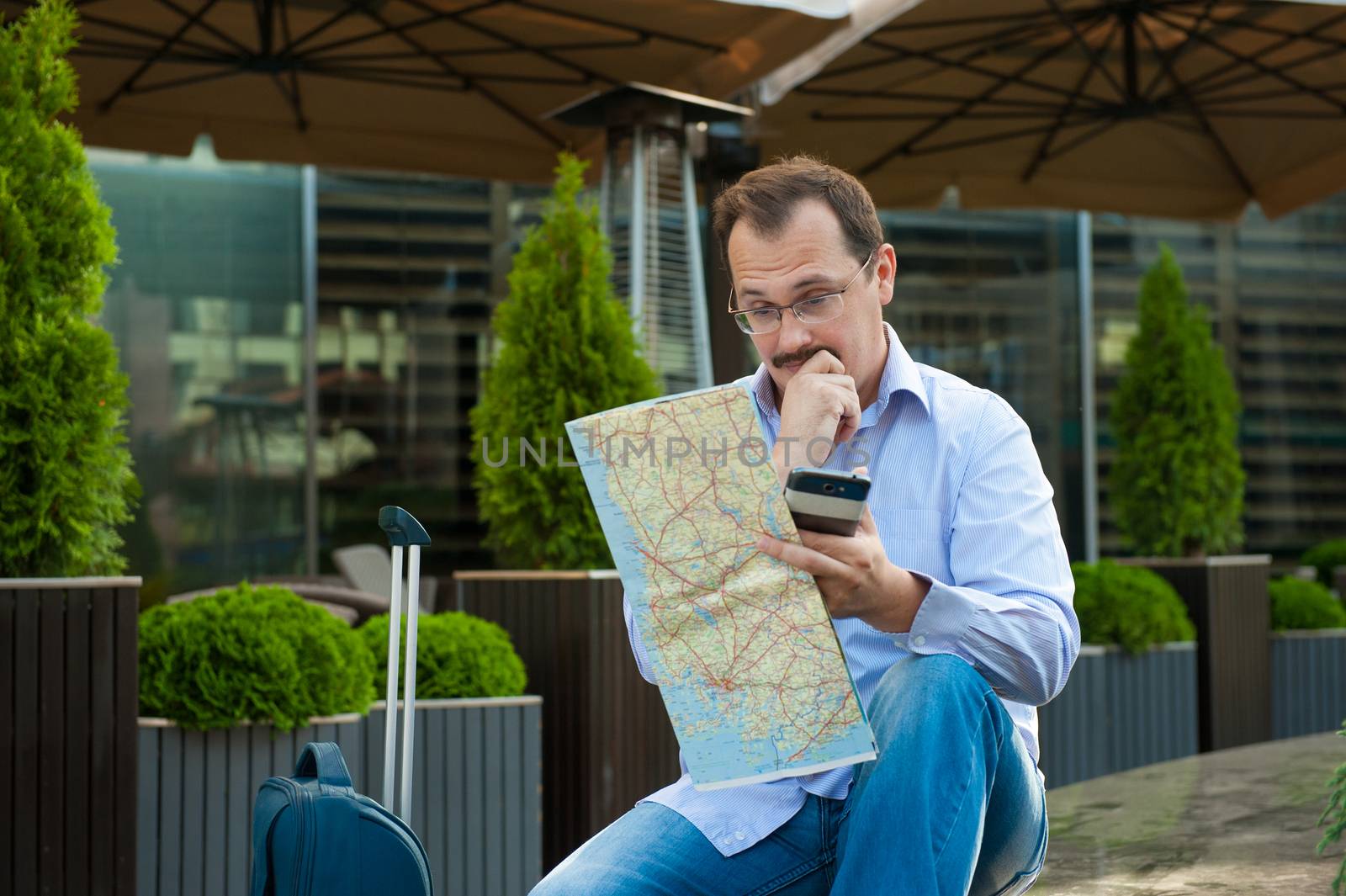 Traveler with mobile phone and city plan sitting outdoors.