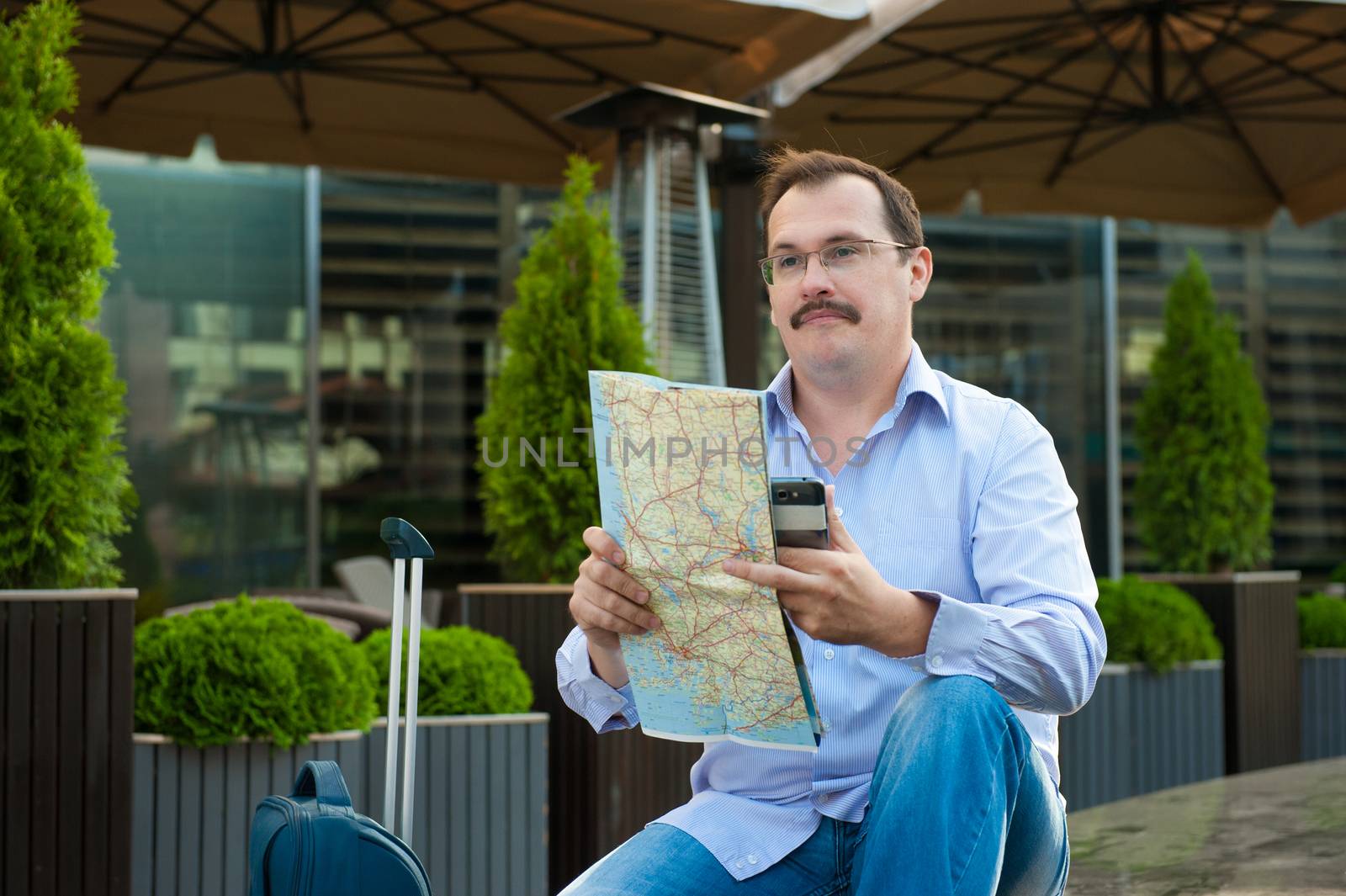 Traveler with mobile phone and city plan sitting outdoors.