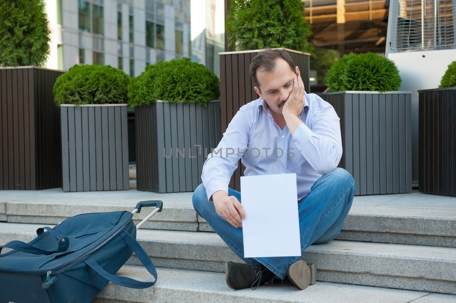 Sad man sitting on the steps with a suitcase Empty sign outdoors