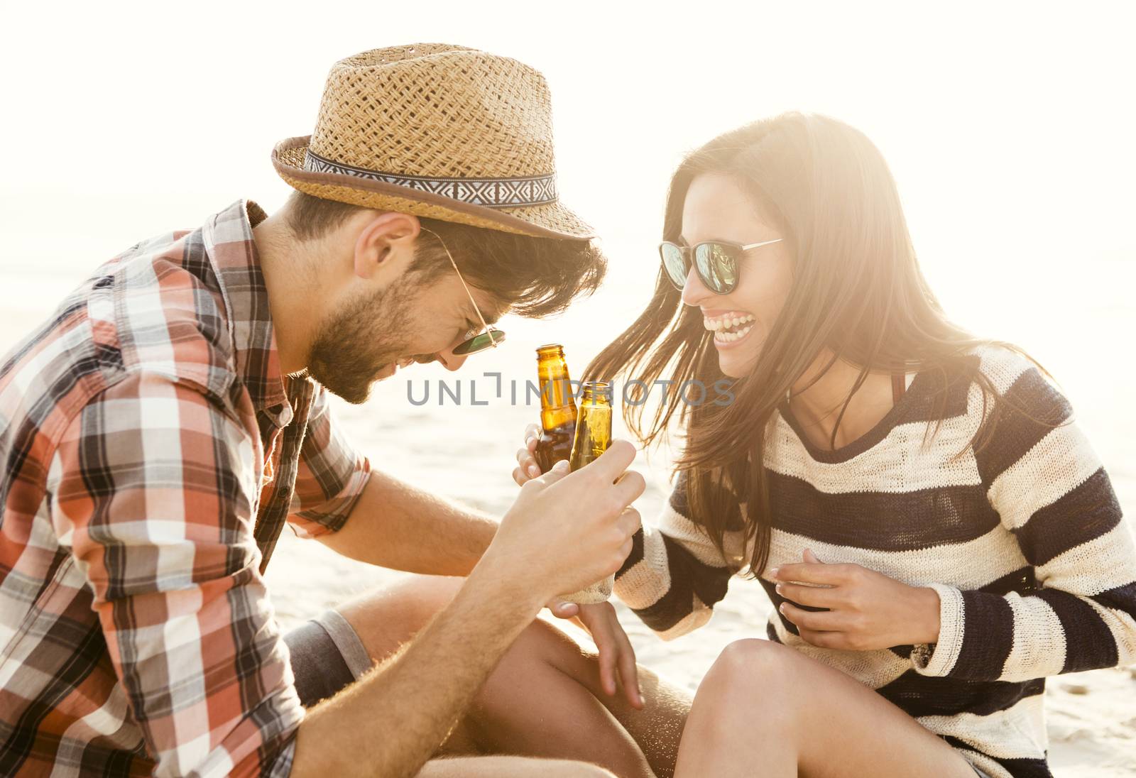 Young couple at the beach having fun, laughing and drinking beer