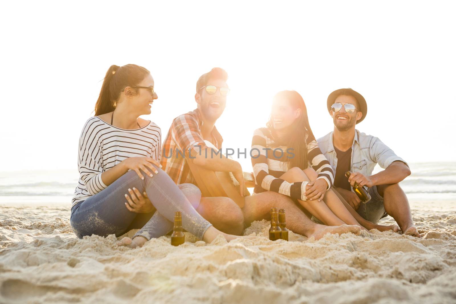 Friends having fun together at the beach, playing guitar and drinking beer