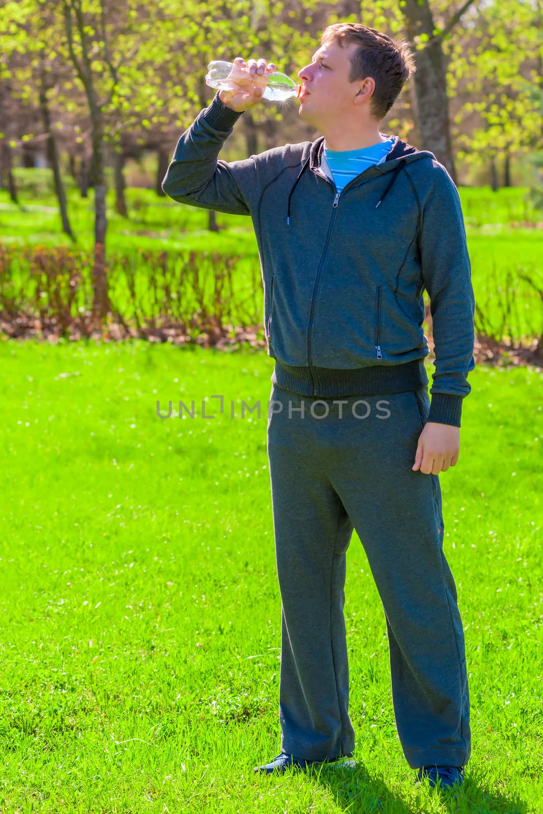 Vertical portrait of a man drinking water on a green lawn