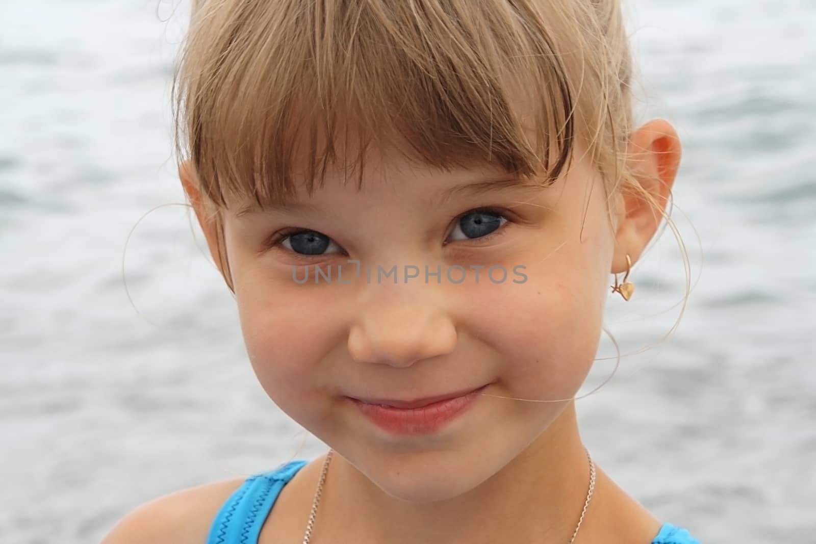 portrait of a smiling blue-eyed baby girl on sea background