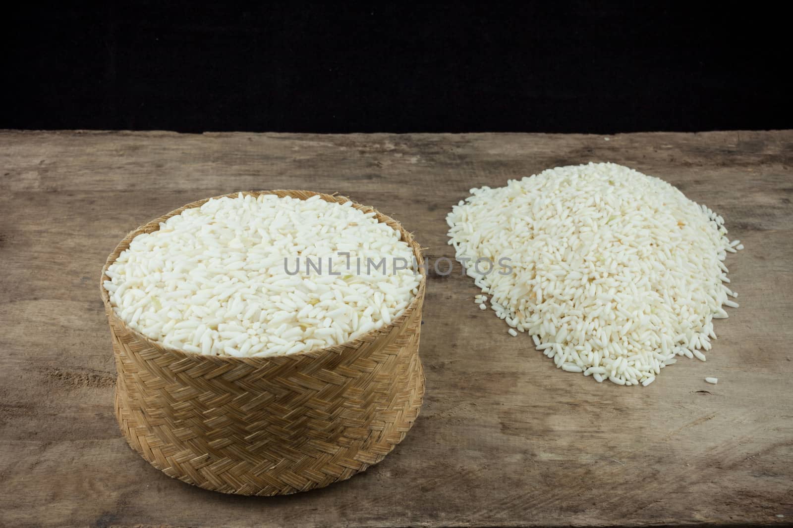 Rice in a wicker rice and scattered near on dark wooden table.