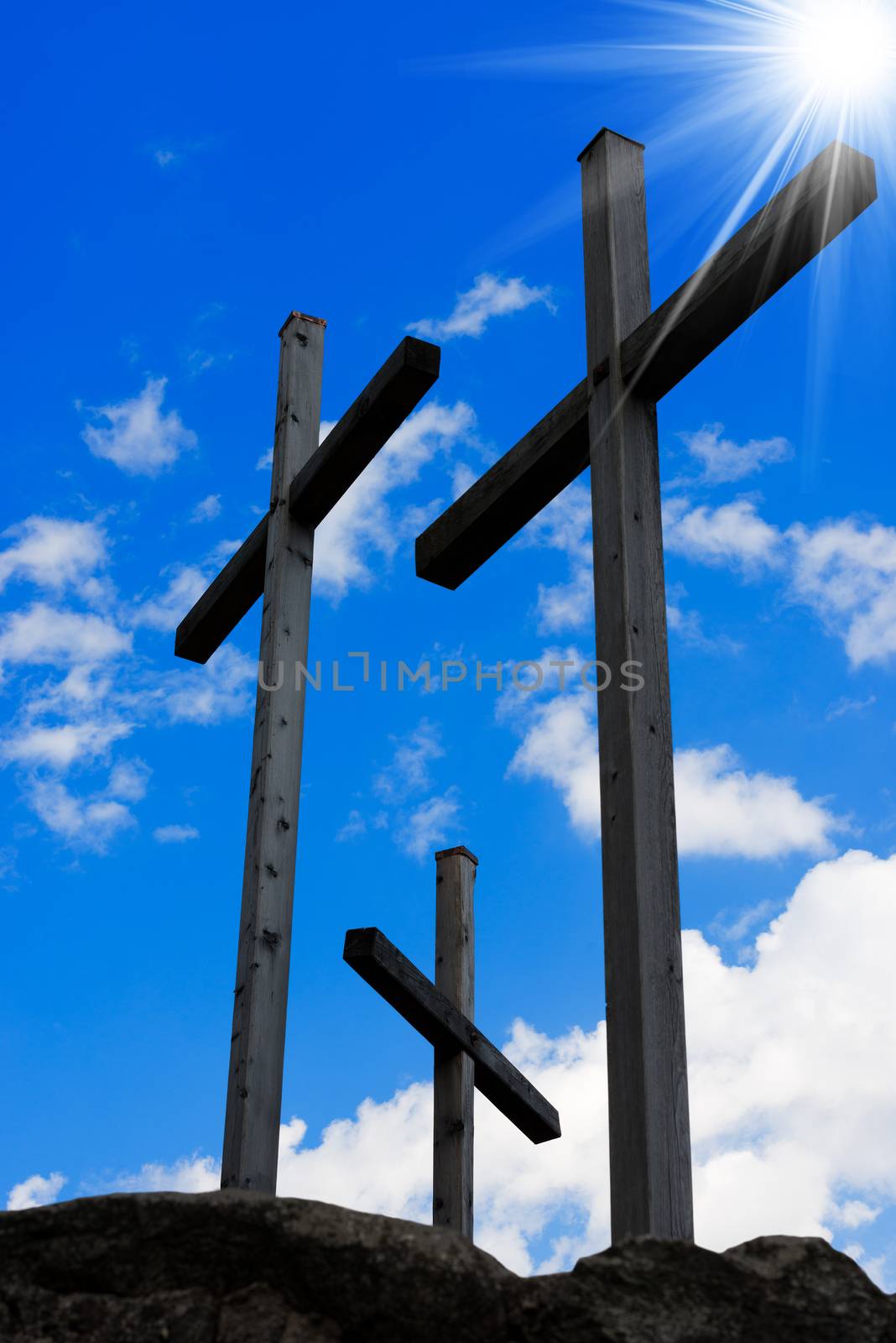 Three wooden crosses on a blue sky with clouds and sun rays on a hill. Symbol of Jesus crucifixion