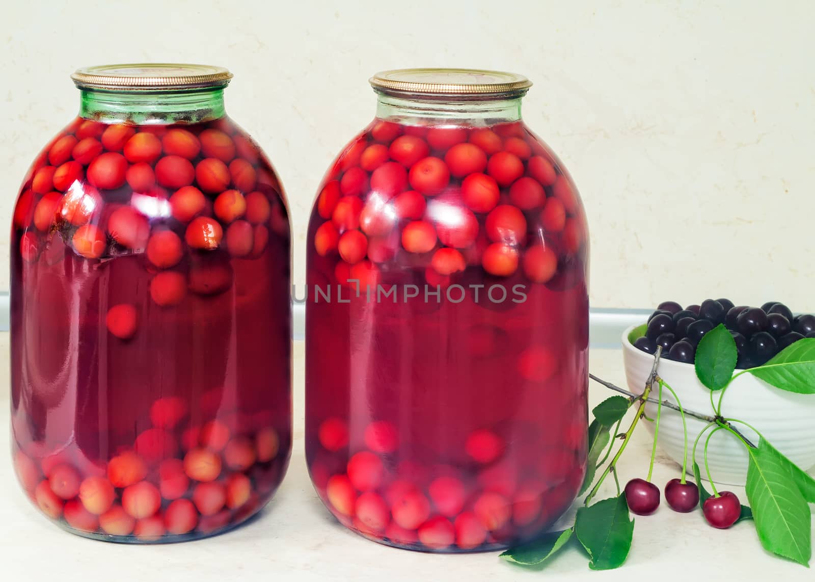 Home canning: large glass cylinders with cherry compote, sealed with metal caps.