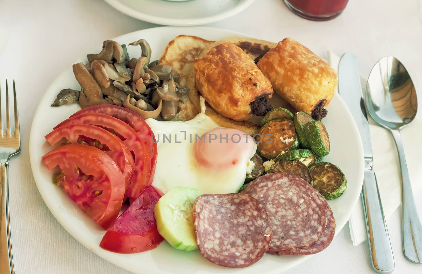 Sliced delicious slices of sausage and scrambled eggs with tomatoes and grilled zucchini on the plate on the table.