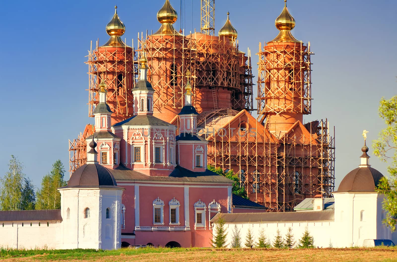 Behind a monastery wall visible to erect a temple with gold domes in scaffolding.