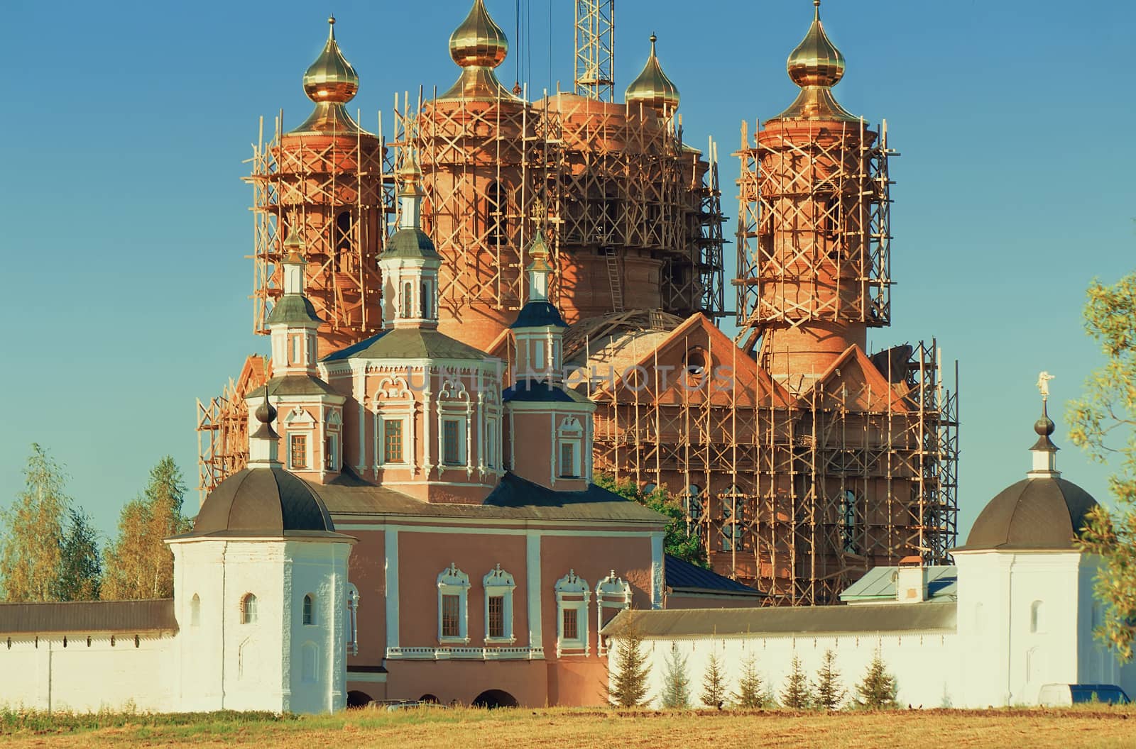 Behind a monastery wall visible to erect a temple with gold domes in scaffolding.
