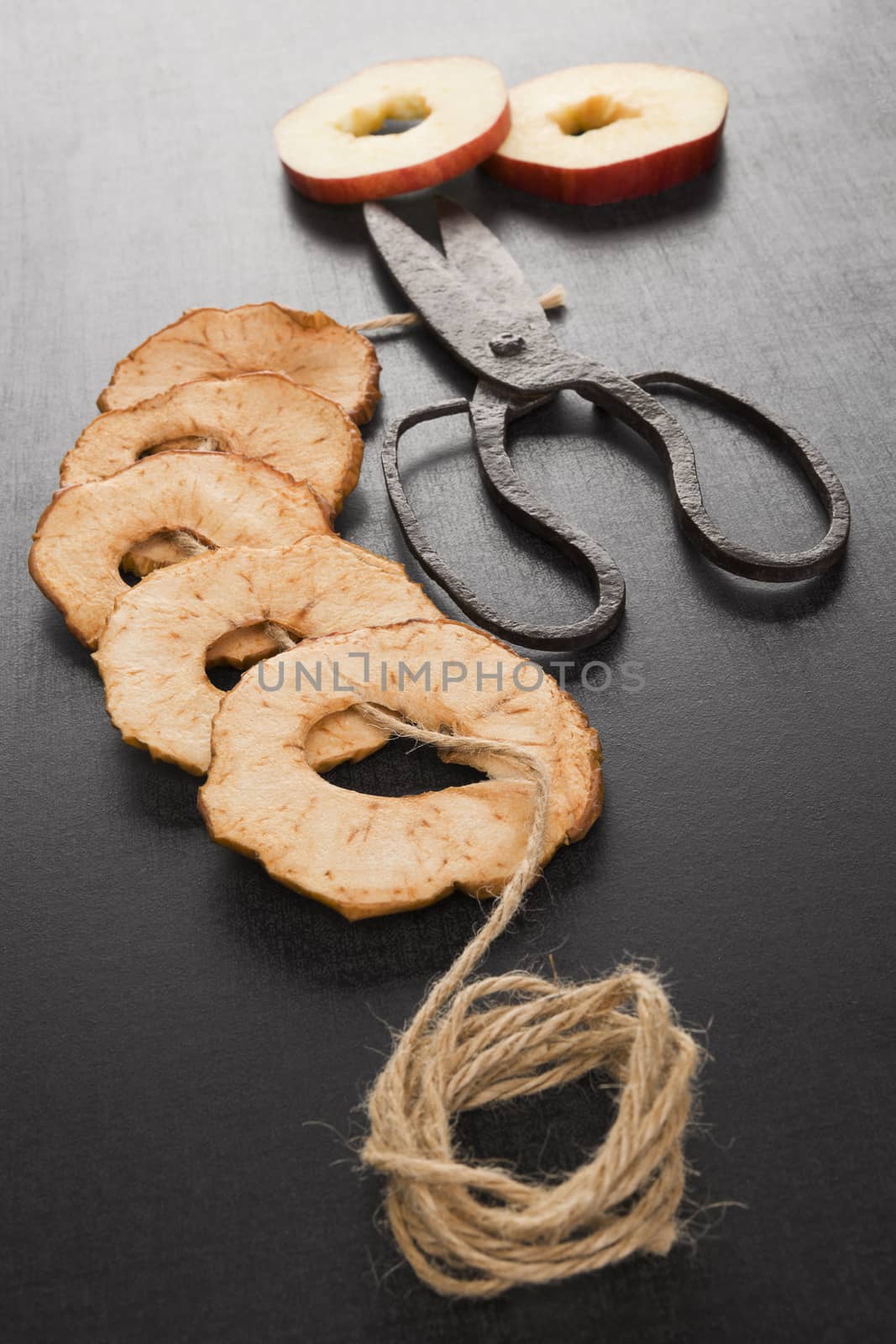 Dry apple chips on black background, with old vintage scissors and natural brown string. Healthy eating, seasonal harvest conservation.